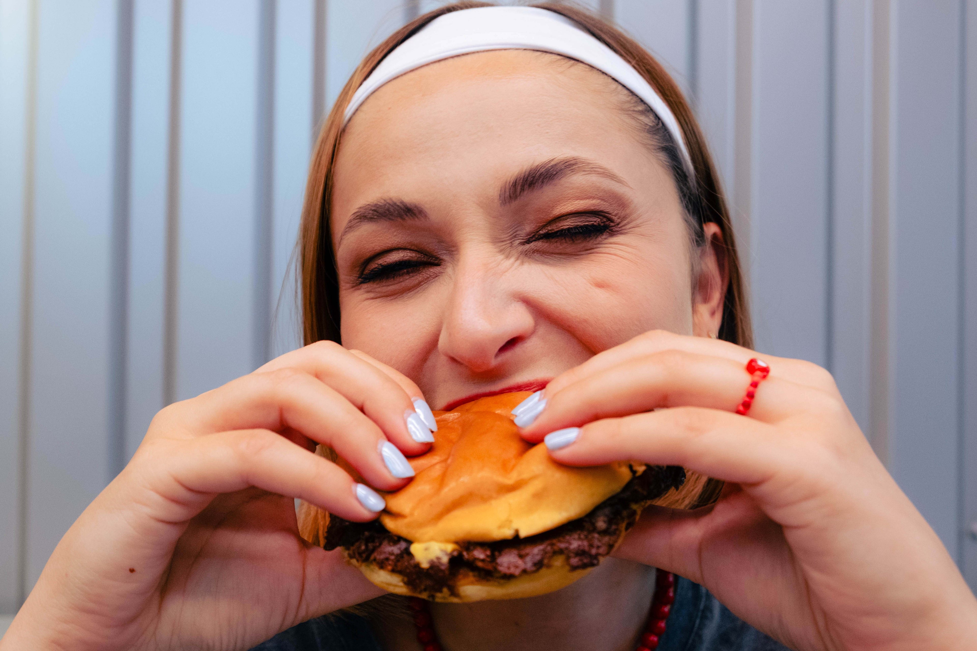 Femme portant une bague rouge Bourjeone en forme de cœur, croquant un burger avec gourmandise – collection Umami.