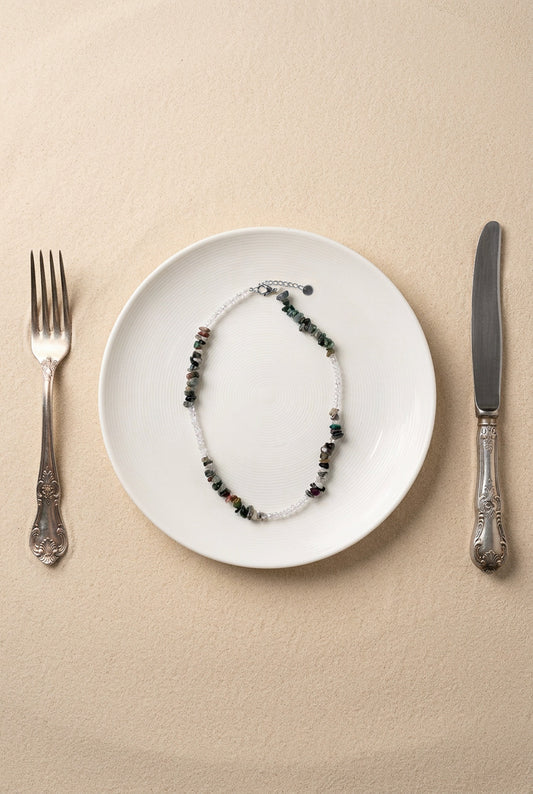 Vue du collier Pistachio sur support noir, mettant en avant les finitions en acier inoxydable doré et les pierres naturelles.