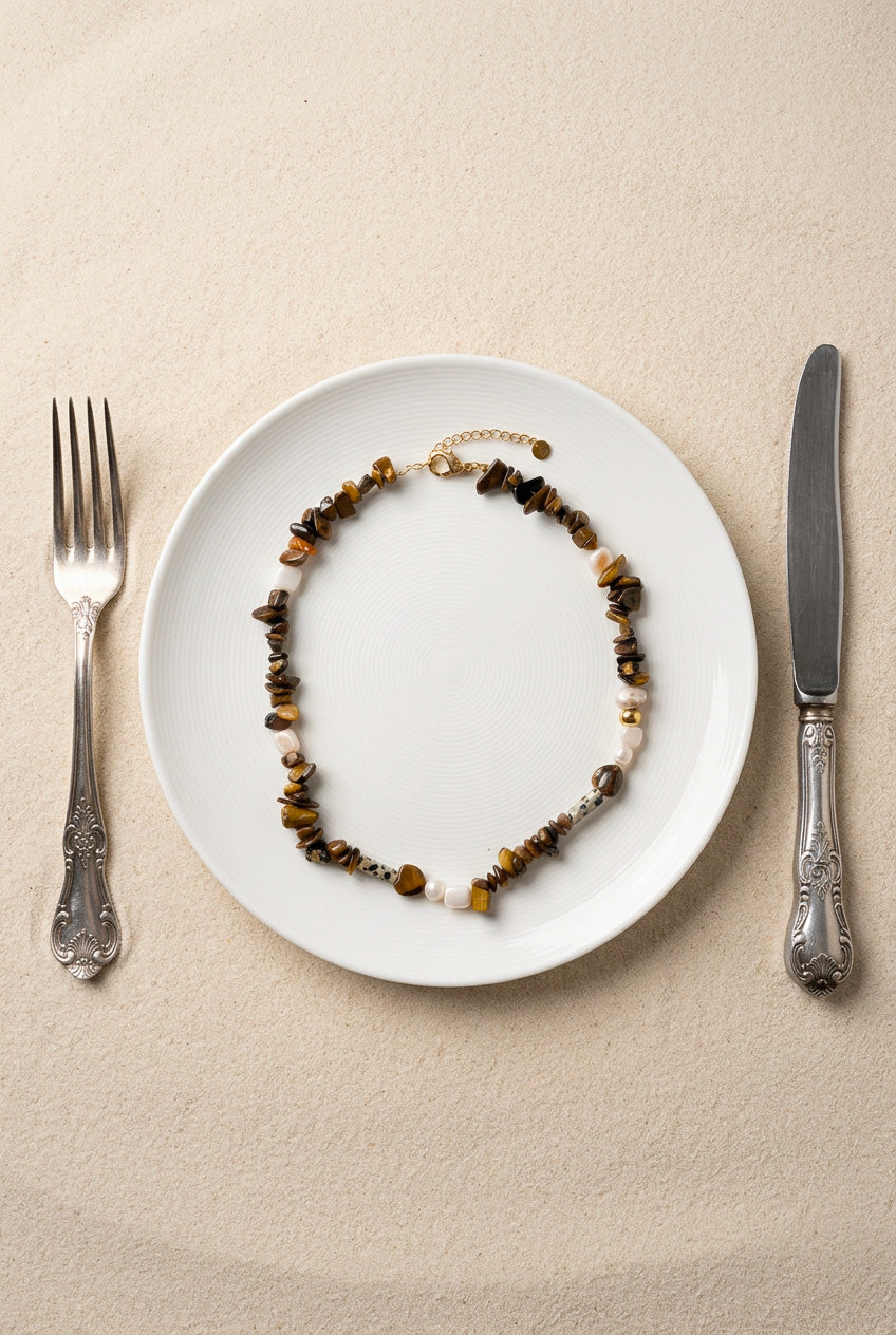 Vue de dessus du collier Nougat présenté dans une assiette blanche, montrant les détails des perles chips œil de tigre, du jaspe dalmatien et des perles d'eau douce.
