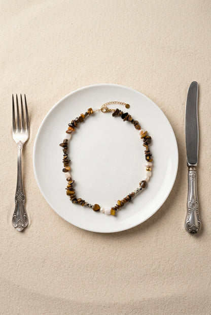 Vue de dessus du collier Nougat présenté dans une assiette blanche, montrant les détails des perles chips œil de tigre, du jaspe dalmatien et des perles d'eau douce.