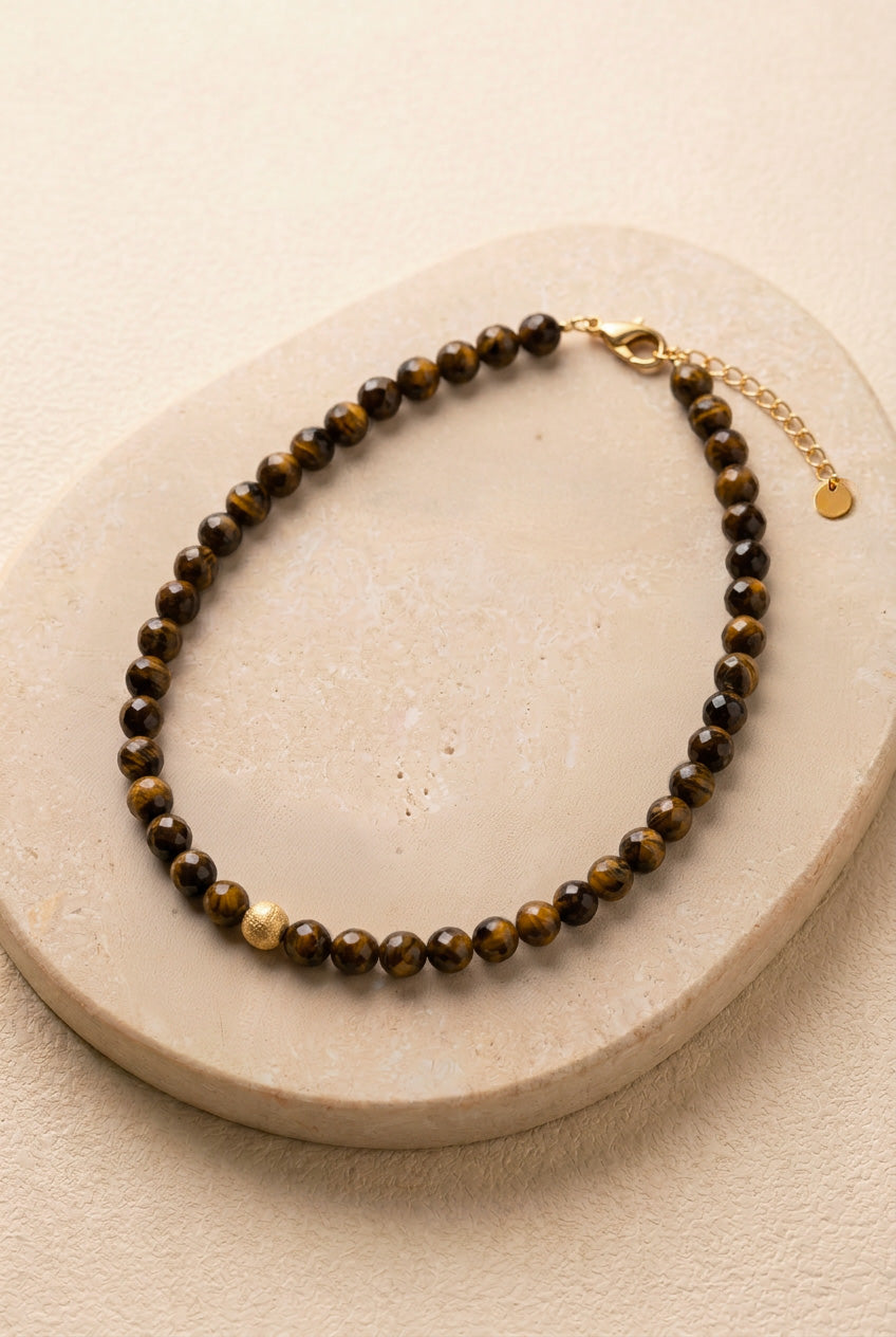Vue détaillée du collier Truffe sur pierre noire, montrant la régularité des perles facettées en œil de tigre et la perle centrale dorée mat.