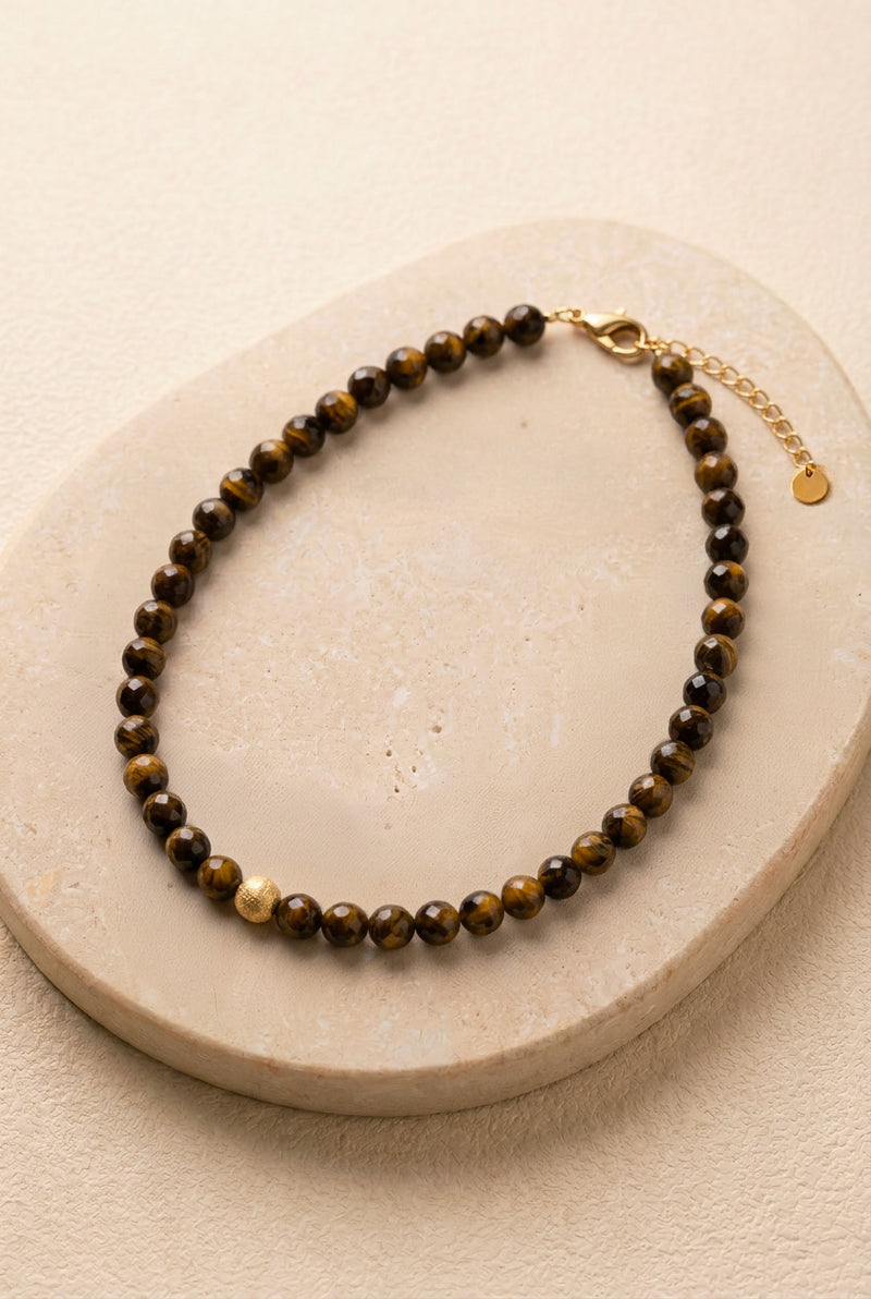 Vue détaillée du collier Truffe sur pierre noire, montrant la régularité des perles facettées en œil de tigre et la perle centrale dorée mat.