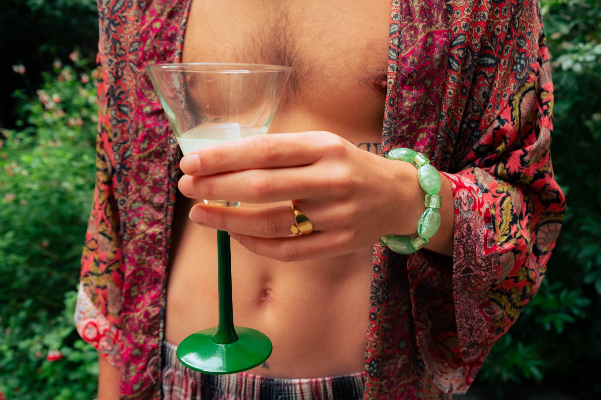 Gros plan sur un poignet portant un bracelet vert Bourjeone tenant un verre dans un jardin.