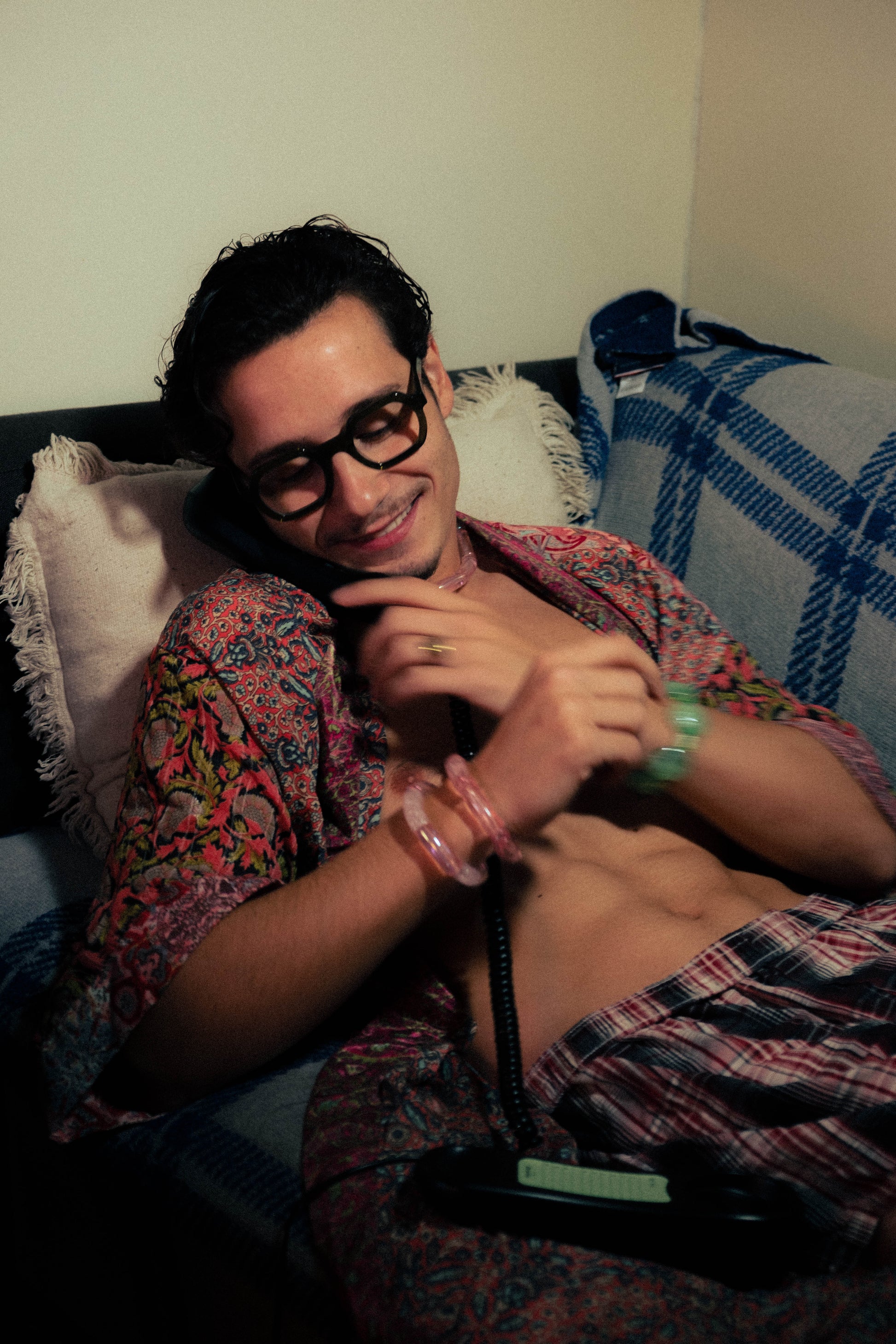 Homme allongé au téléphone portant des bracelets colorés Bourjeone dans une ambiance rétro et douce.