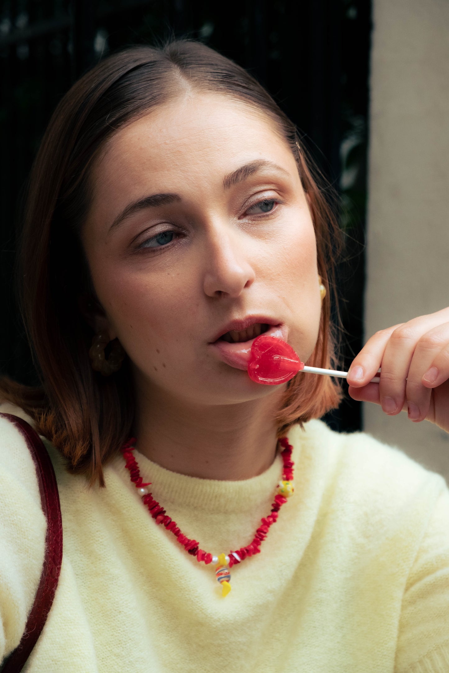 Femme portant un collier rouge Bourjeone et dégustant une sucette en forme de cœur.