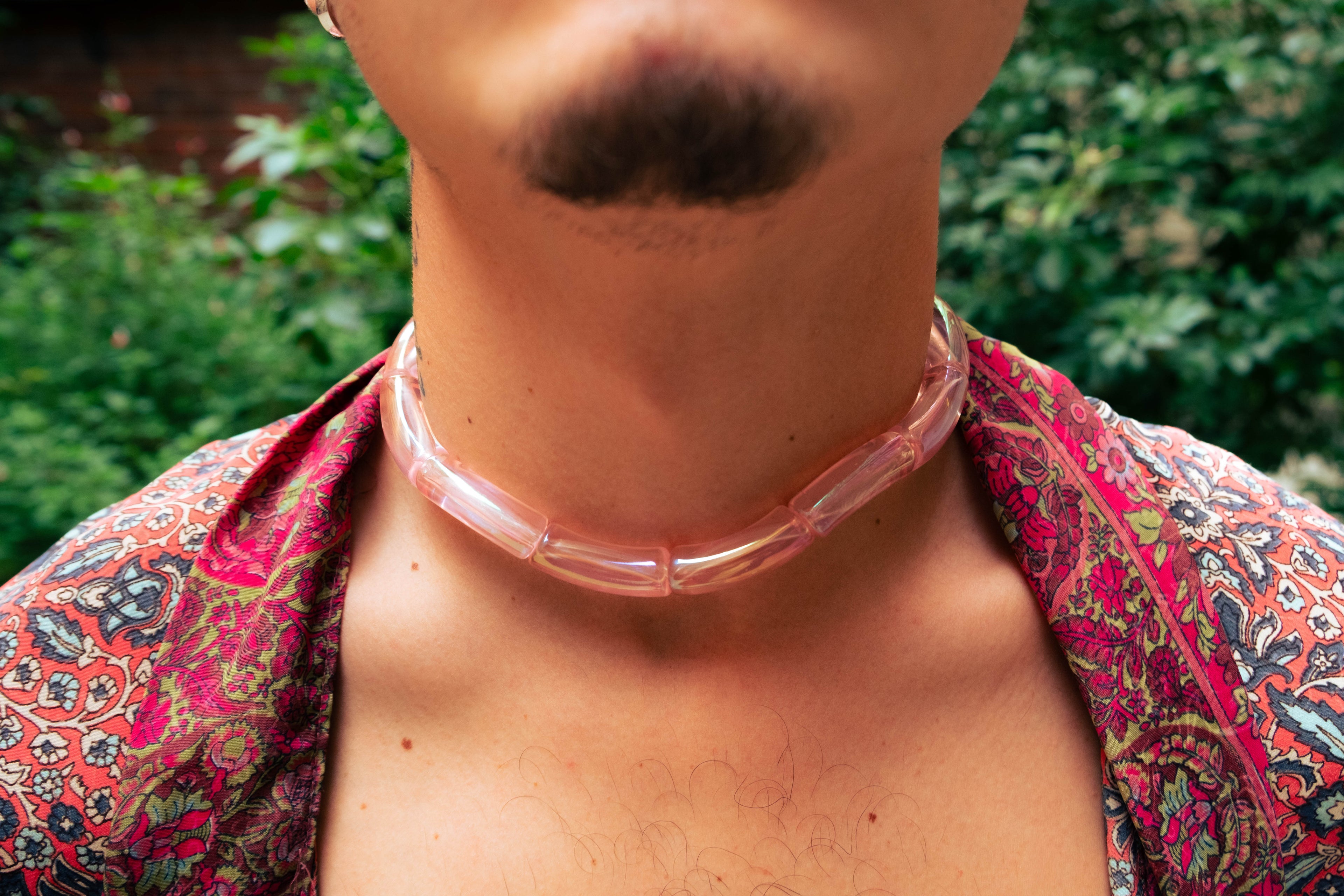 Gros plan sur un collier rose translucide Bourjeone porté sur une chemise imprimée colorée.