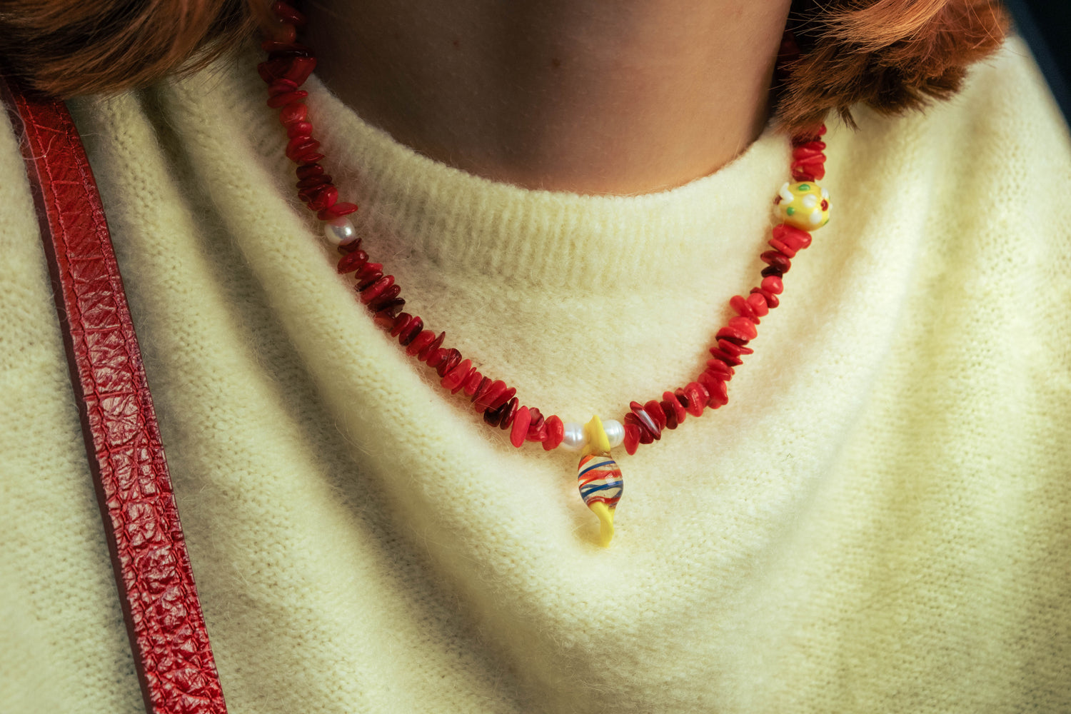 Gros plan sur un collier rouge Bourjeone avec perles colorées porté sur un pull jaune pâle.