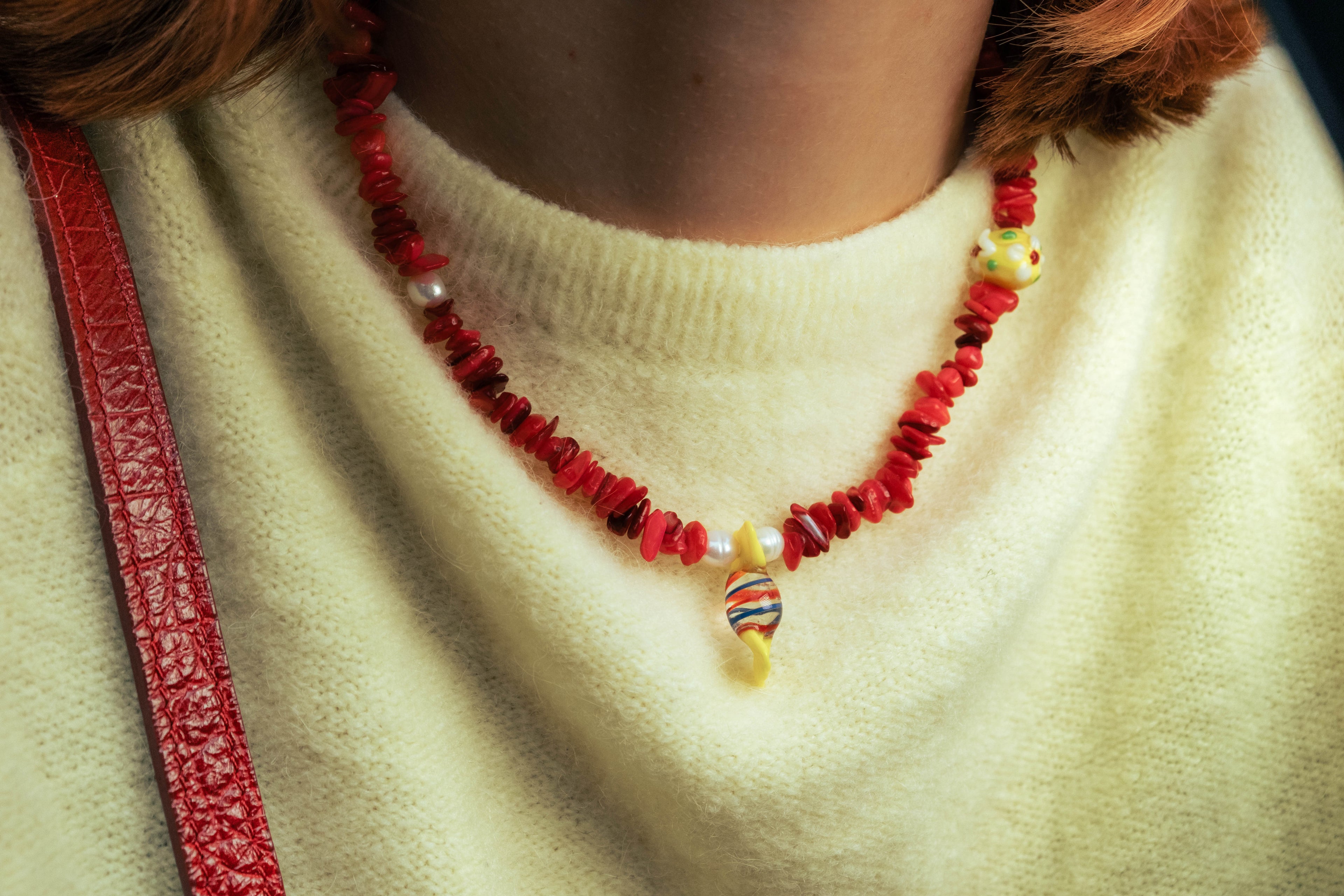 Gros plan sur un collier rouge Bourjeone avec perles colorées porté sur un pull jaune pâle.