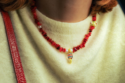 Gros plan sur un collier rouge Bourjeone avec perles colorées porté sur un pull jaune pâle.