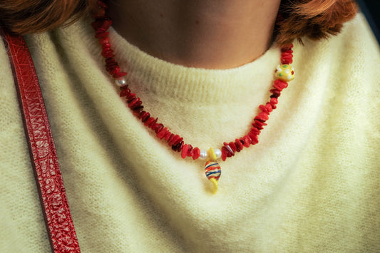 Gros plan sur un collier rouge Bourjeone avec perles colorées porté sur un pull jaune pâle.