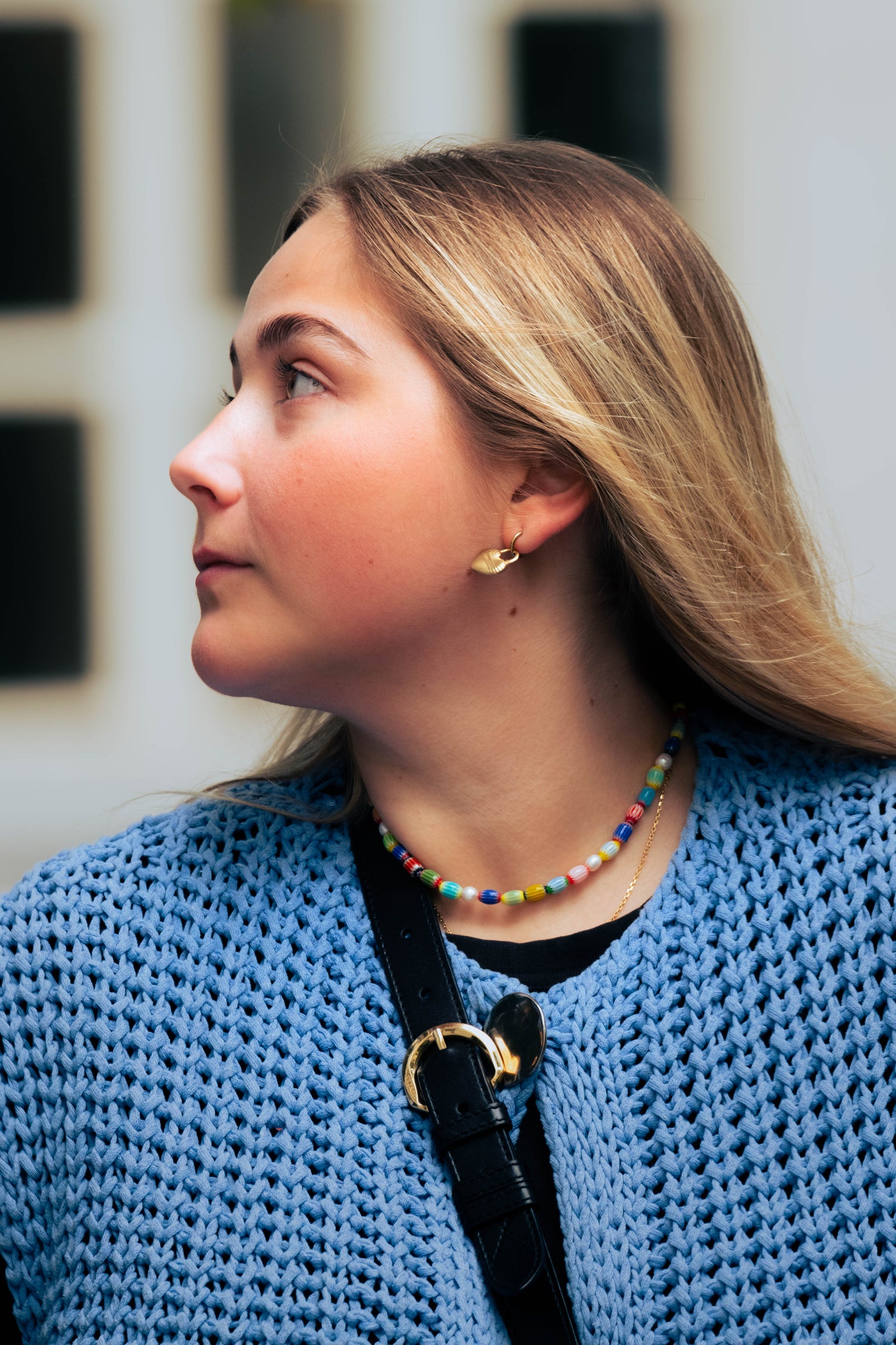 Portrait d’une femme portant un collier coloré Bourjeone et des boucles d’oreilles dorées.