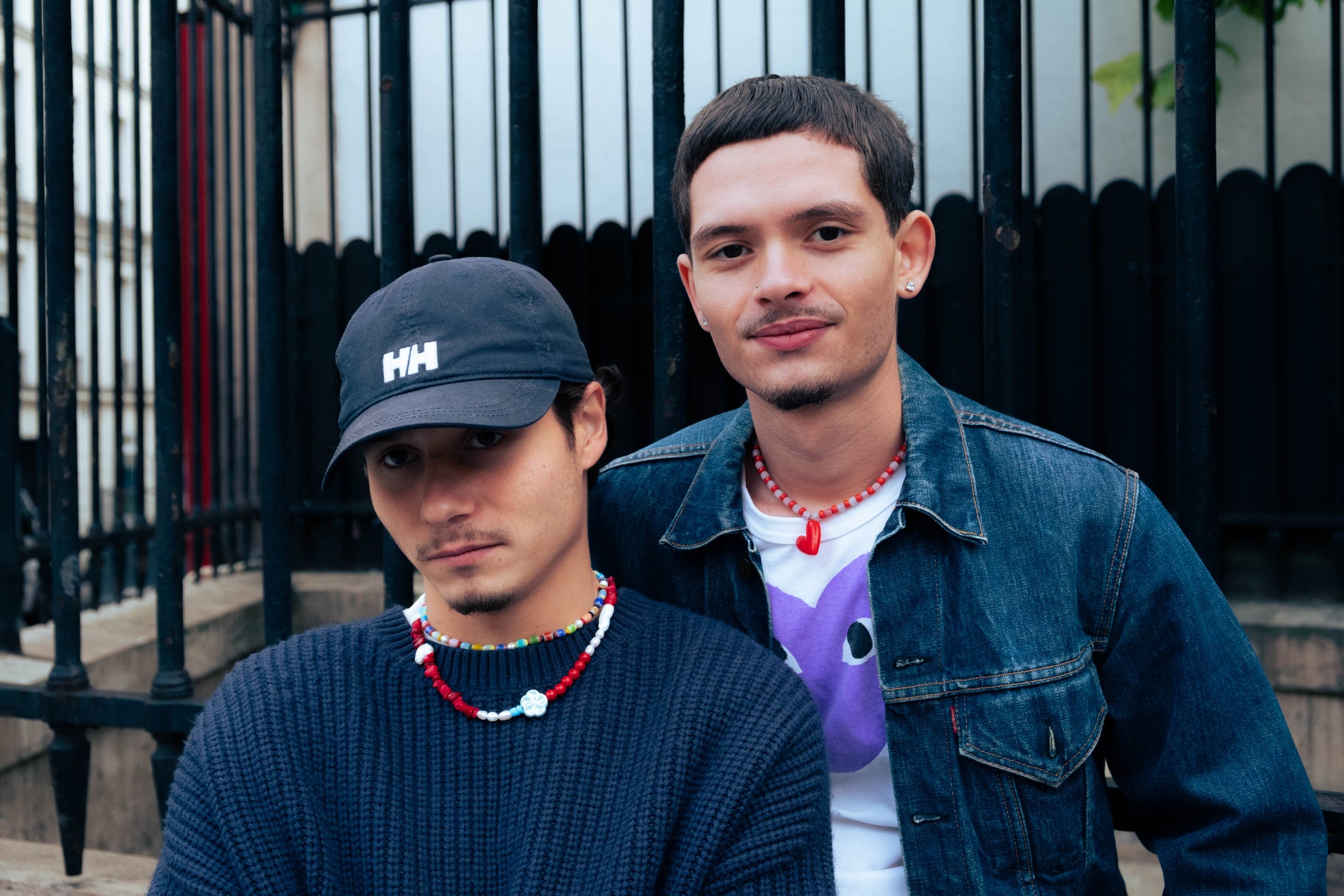 Deux hommes à Paris portant des colliers Bourjeone rouges et colorés devant une grille noire.