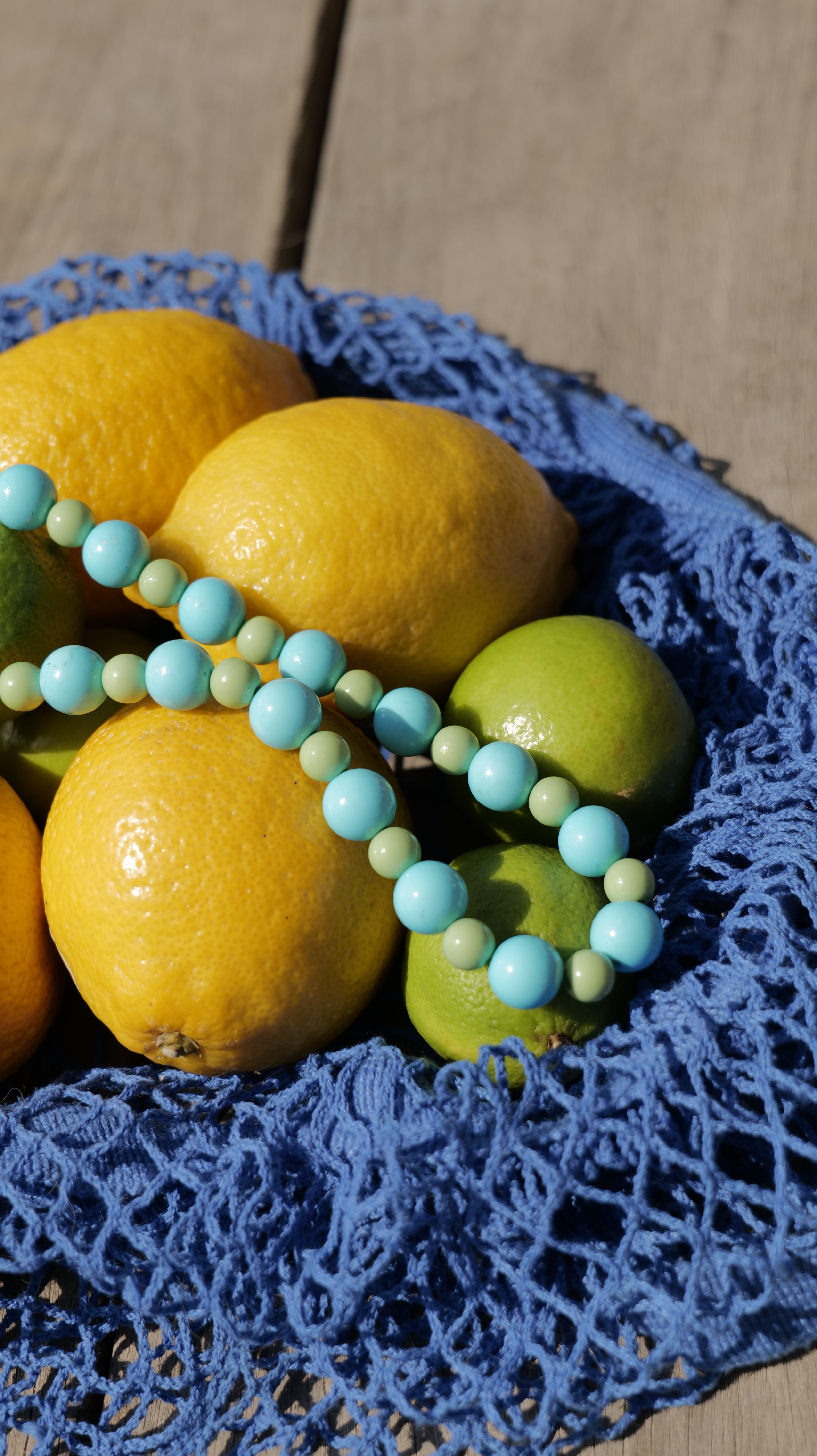 Bracelet Bourjeone turquoise et vert en perles, photographié sur des citrons et des limes – collection Acidulée.