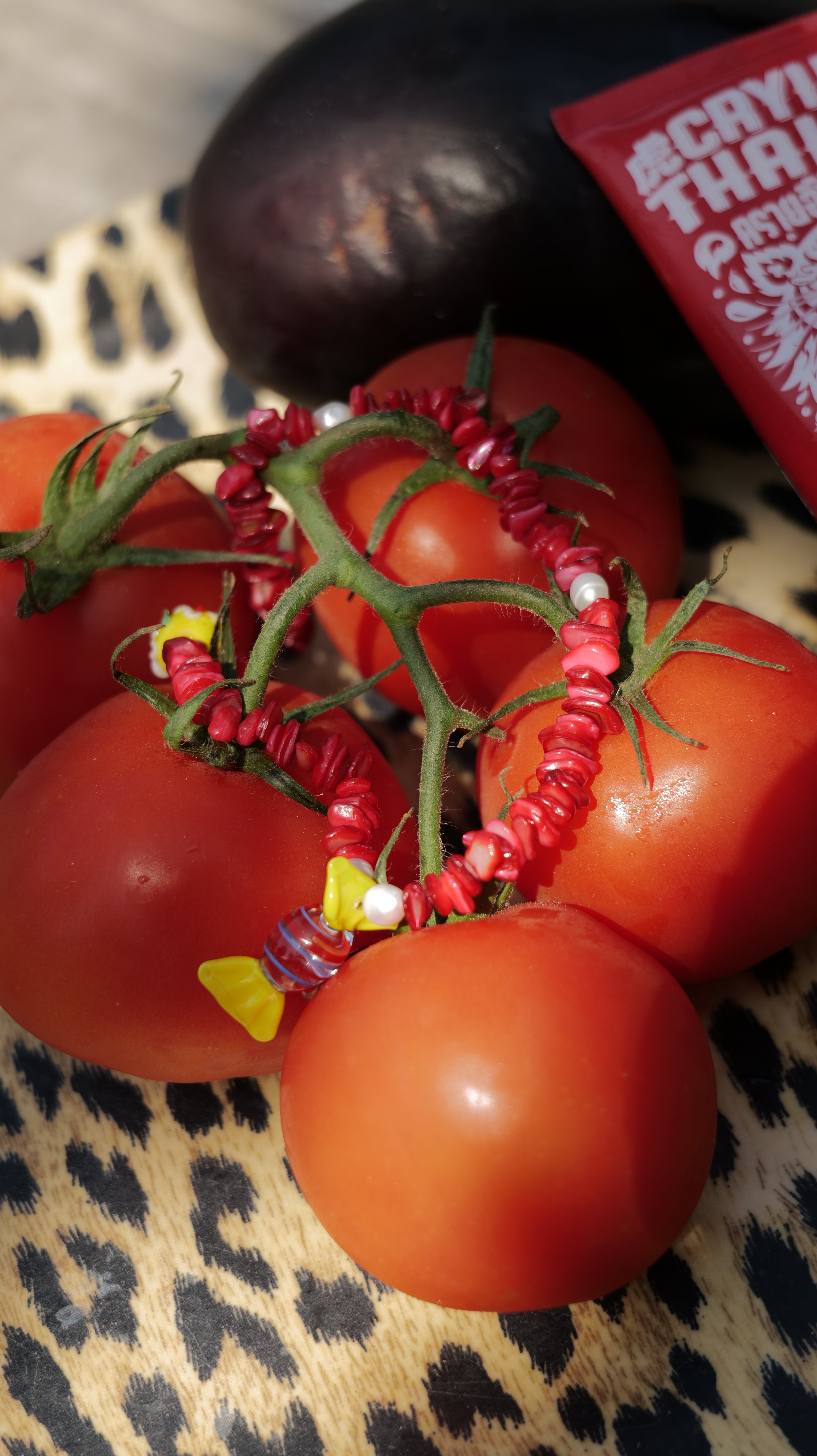 Bracelet Bourjeone rouge en perles artisanales, photographié sur des tomates avec un piment – collection Vitaminée: