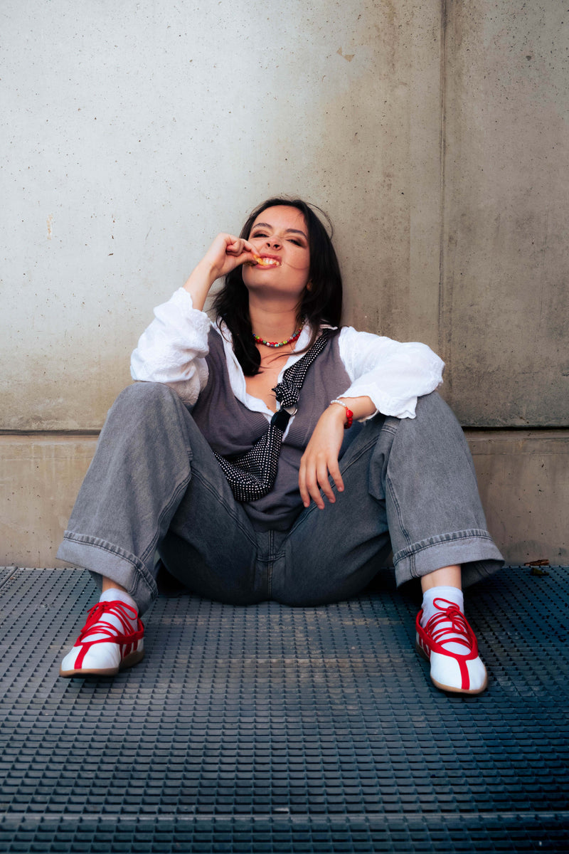 Femme assise au sol portant un collier Bourjeone en perles colorées et un bracelet rouge, dégustant des frites avec audace – collection Umami.