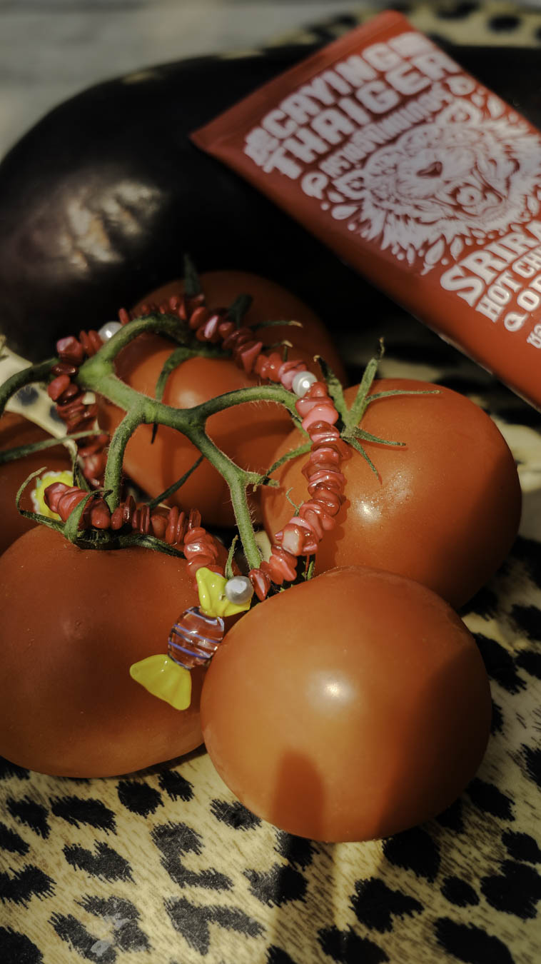 Collier Bonbonnière Bourjeone posé sur des tomates, bijou fait main aux perles rouges et pendentif bonbon en verre, ludique et gourmand.