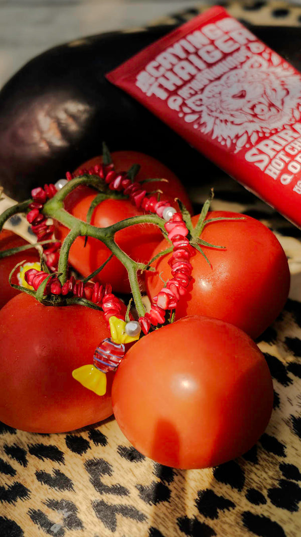 Collier Bonbonnière Bourjeone posé sur des tomates, bijou fait main aux perles rouges et pendentif bonbon en verre, ludique et gourmand.