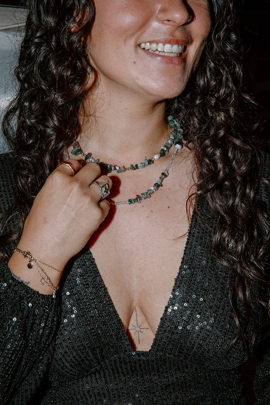 Une femme riant lors d'une soirée, l'une portant le collier Câpre en pierres vertes, illustrant un style chic et festif.