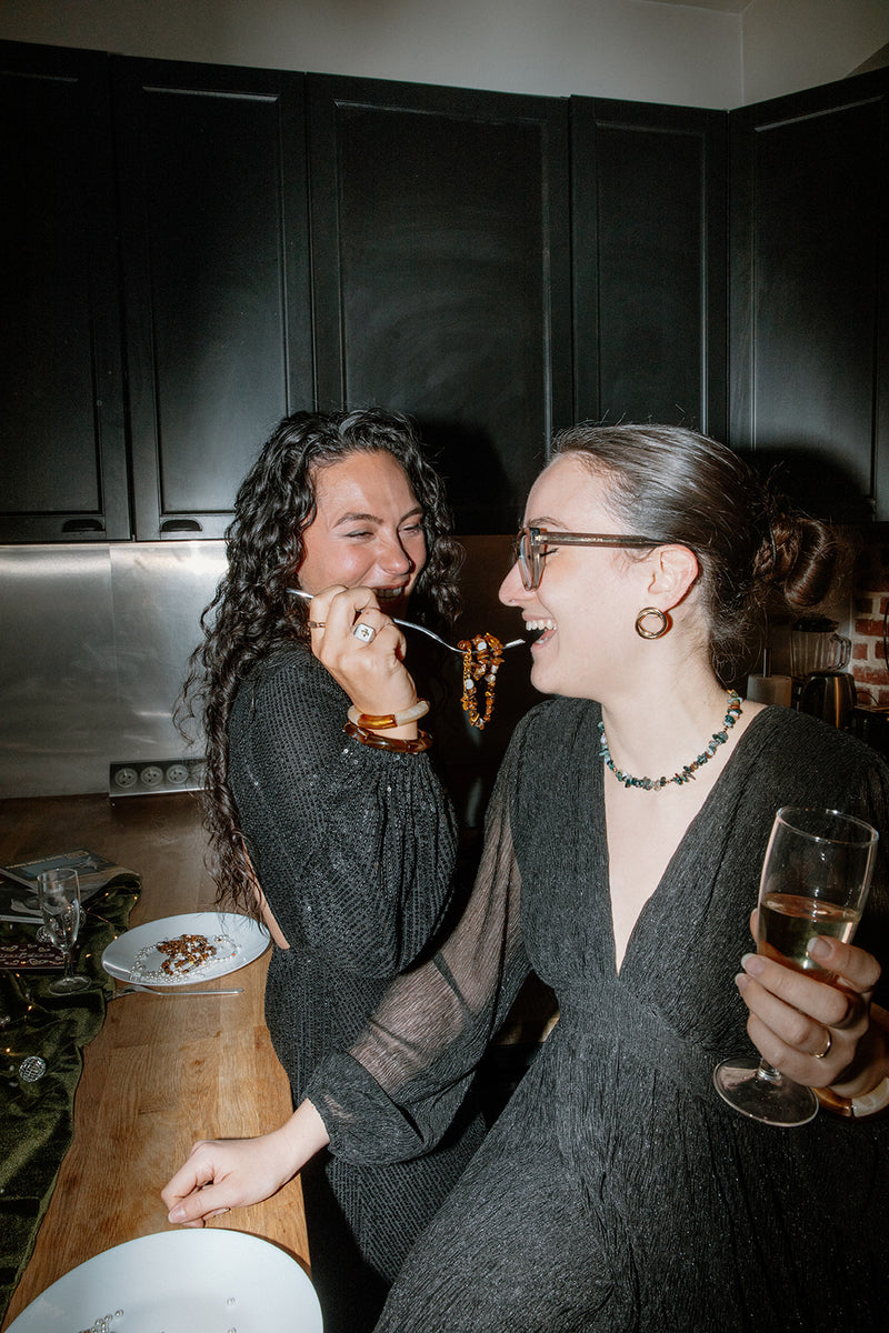 Deux femmes riant lors d'une soirée, l'une portant le collier Câpre en pierres vertes, illustrant un style chic et festif.