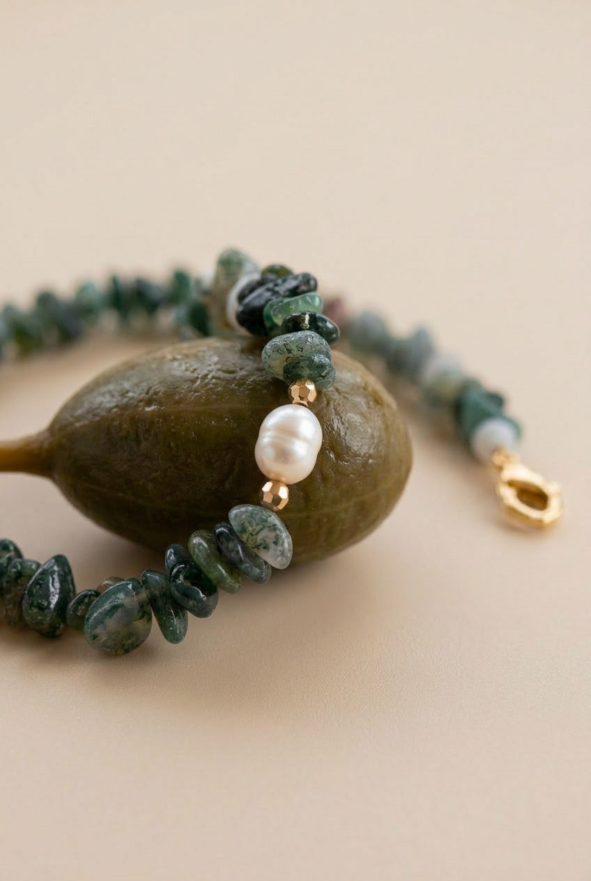 Gros plan macro du collier Câpre avec pierres naturelles vertes et perle d'eau douce posé sur une câpre, bijou artisanal de la Collection Salée.