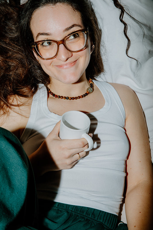 Portrait d'une femme portant le collier Gravy avec débardeur blanc et tenant un mug, montrant les reflets de la perle strass au flash.