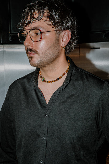 Plan moyen d'un homme portant le collier Gravy par-dessus une chemise noire, soulignant le caractère unisex et élégant du bijou.