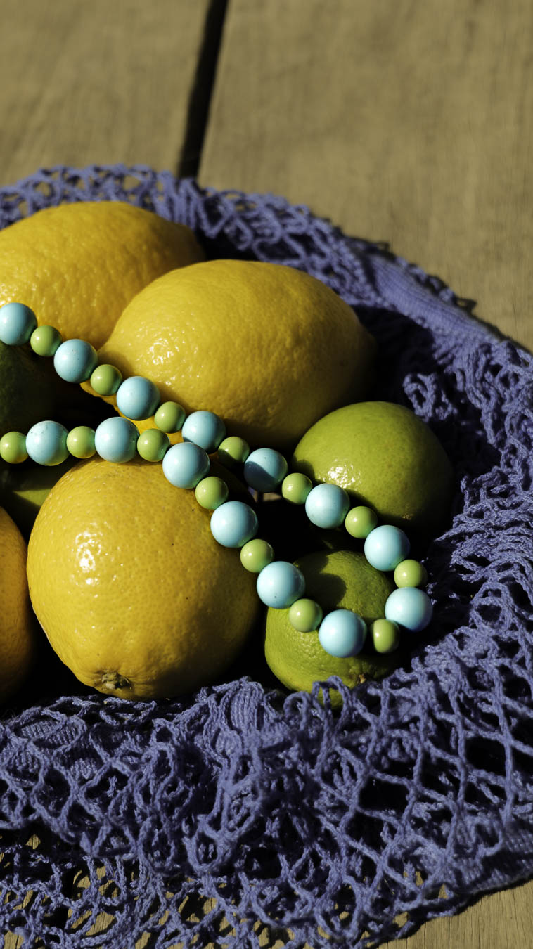 Collier Mojito Bourjeone posé sur des citrons jaunes et verts, bijou fait main aux perles bleu lagon et vert menthe, frais et estival.