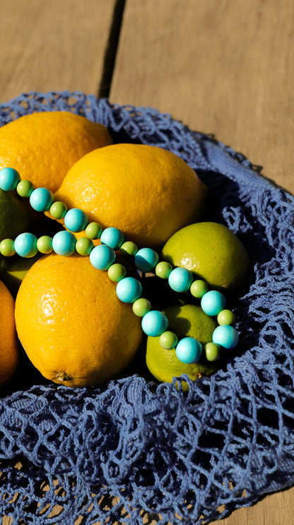 Collier Mojito Bourjeone posé sur des citrons jaunes et verts, bijou fait main aux perles bleu lagon et vert menthe, frais et estival.