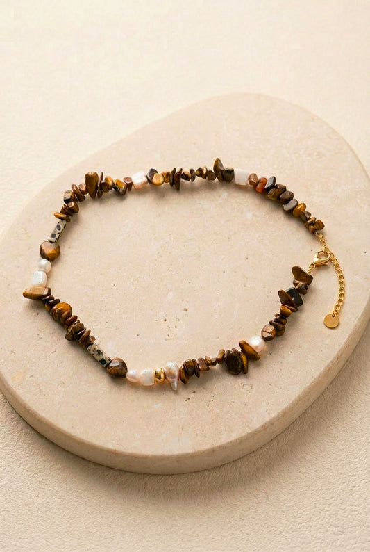 Packshot du collier Nougat posé sur un support en pierre noire, mettant en valeur les textures des pierres naturelles et les finitions en acier inoxydable doré.