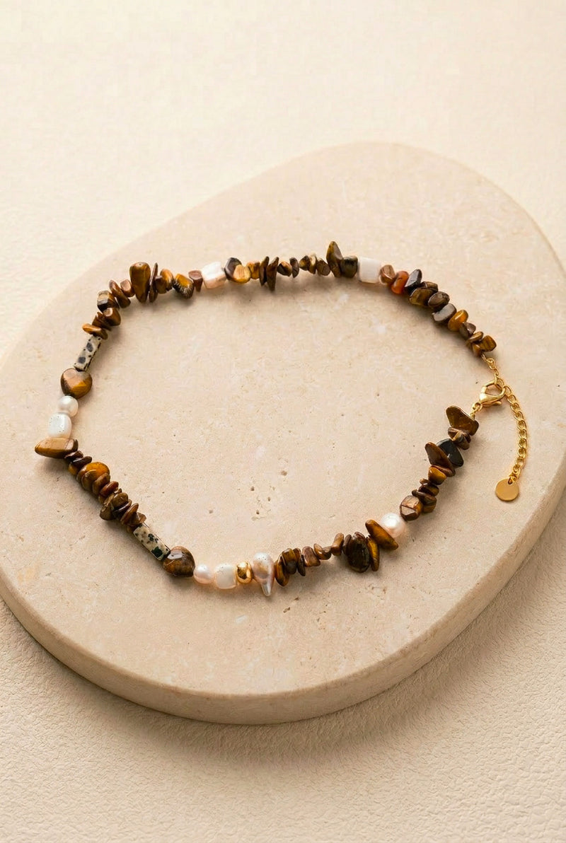 Packshot du collier Nougat posé sur un support en pierre noire, mettant en valeur les textures des pierres naturelles et les finitions en acier inoxydable doré.