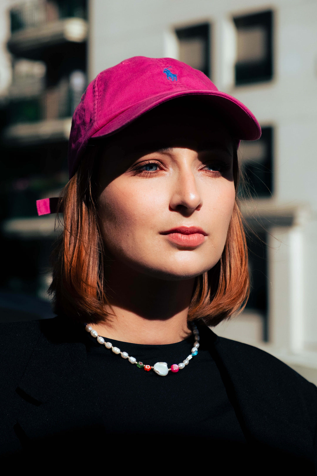 Femme portant un collier de perles blanches et colorées Bourjeone avec une casquette fuchsia – collection Vitaminée.